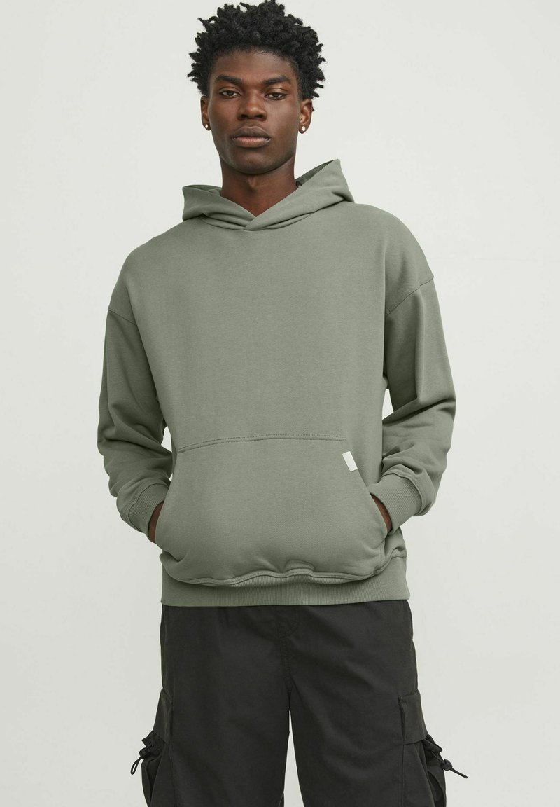Sudadera verde oliva hecha de una tela suave, con un bolsillo frontal, puños acanalados y capucha ajustable. Ajuste casual con un branding mínimo.