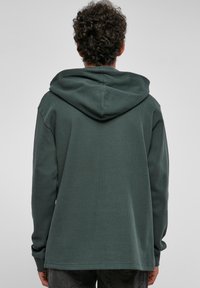 Felpa verde scuro con tessuto a trama, maniche lunghe e vestibilità morbida. Caratterizzata da un ampio cappuccio e un orlo dritto sul retro.