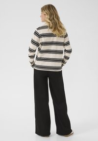 Cămașă cu mâneci lungi în dungi de culoare crem cu dungi orizontale negre, combinată cu pantaloni negri largi și încălțăminte bej.