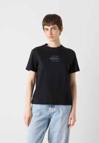 Zwarte katoenen t-shirt met korte mouwen en ronde hals, met een witte opdruk van het logo "Calvin Klein" en symbool op de voorkant.