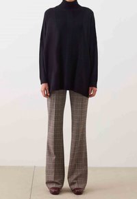 Czarny oversize'owy sweter z golfem o fakturowanym pionowym wzorze, zestawiony z brązowymi, plisowanymi spodniami w kratę oraz brązowym obuwiem. Prosty, nowoczesny design.