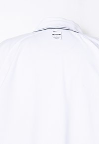 Bela polo majica Nike, ki prikazuje zadnji ovratnik z etiketo, na kateri piše o sklapanju ohlapno in narejeno v Kambodži.