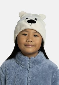 Gorro de punto blanco con relieve y orejas de oso, detalles de ojos y nariz negros. Se lleva con una chaqueta de cremallera de felpa azul claro.