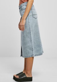 Lys blå denim midi-skjørt med rett snitt, sidespalte og synlige sømmer. Kombinert med enkle svarte platåsandaler.