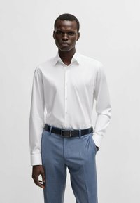 Witte langemouw overhemd met een gestructureerde kraag, gecombineerd met lichtblauwe op maat gemaakte broek en een donkerblauwe riem. Glad stofafwerking.