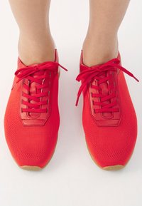 Scarpe atletiche rosse realizzate in materiali mesh e pelle, con punta arrotondata, lacci anteriori e superficie testurizzata. Suola in gomma.
