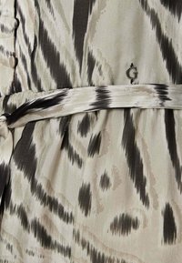 Abito caratterizzato da un motivo ikat beige e nero, con cintura annodata in vita e dettagli botton. Realizzato in un tessuto morbido con una texture delicata.