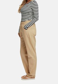 Randig långärmad skjorta i svart och vitt, tillsammans med beige byxor med elastisk midja och vita sandaler med flexibel sula.