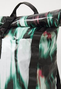 Sac à dos à rabat avec un design à motifs noir, vert et blanc, fabriqué en matériau durable avec des bretelles noires ajustables et une quincaillerie.