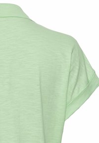 Lichtgroen polo shirt met korte mouwen van een gestructureerde stof. Beschikt over een geribde kraag en opgerolde mouwen, wat de casual uitstraling benadrukt.