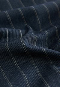 Tissu bleu marine avec de fines rayures verticales dans une teinte plus claire. Le matériau a une finition lisse et texturée typique du denim.