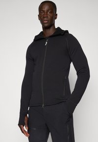 Black zip-up hoodie made of a soft fabric, featuring a fitted design, hood, and thumbholes on the cuffs. Smooth texture with minimal detailing.