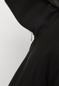 Svart zipparjacka med hög krage. Har slät tygkvalitet, silverfärgad zipparutrustning och en figurvänlig design.