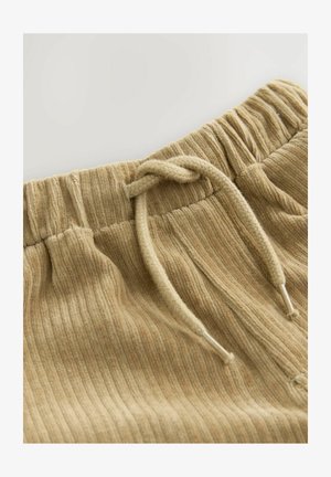 Pantaloni jogger de culoare bej deschis, cu textil ribat și talie elastică, echipați cu un șnur de ajustare. Suprafață texturată cu variații subtile de culoare.