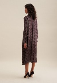 Lungo vestito floreale nero con motivi multicolor, presenta maniche lunghe e una vestibilità comoda, abbinato a tacchi alti neri.