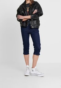 Svart skinnbikerjacka, mörka denimkorta byxor och vita höga sneakers. Enkel design, texturerade material och avslappnad stil.