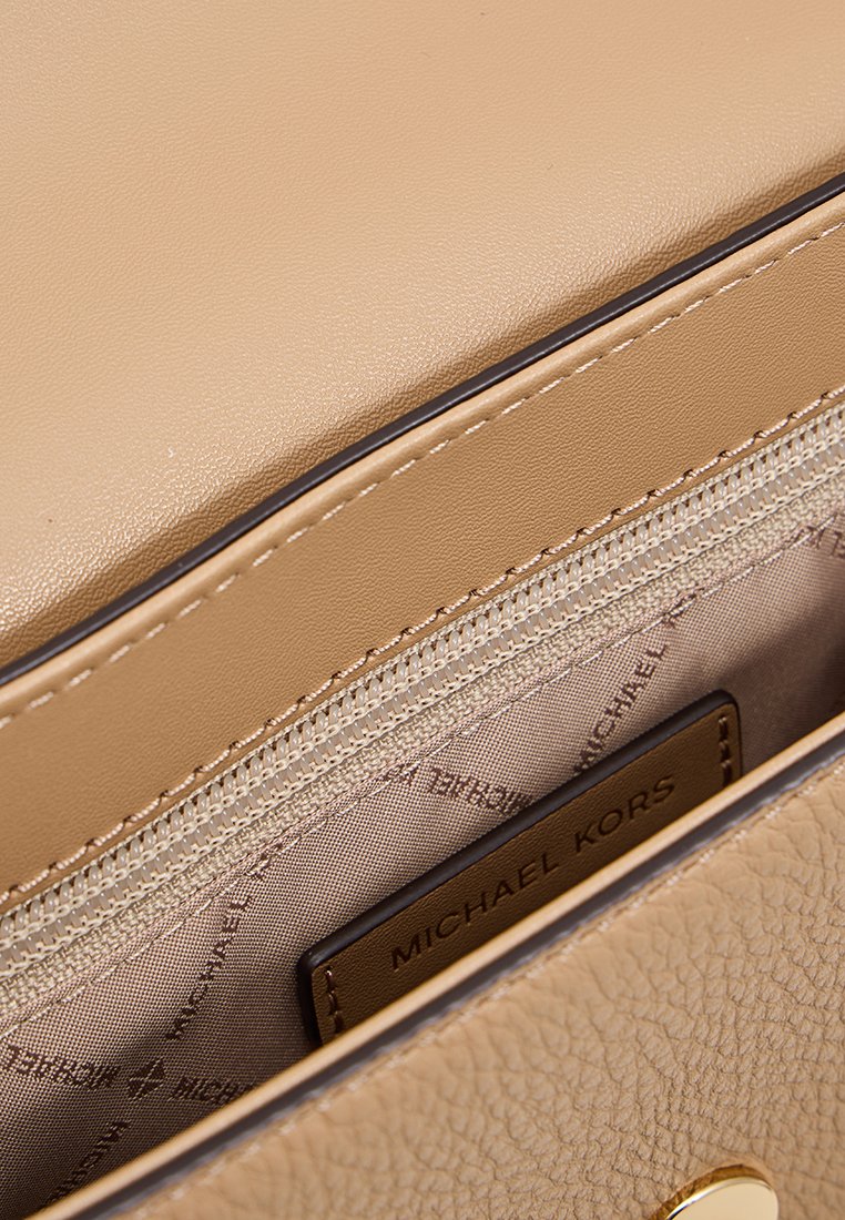 Close-up van de binnenkant van een beige lederen handtas, met een ritszak en het Michael Kors-logo op de stoffen voering en leren label.