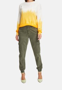 Bawełniany sweter w gradientzie od białego do żółtego, zestawiony z oliwkowymi spodniami cargo. Akcenty to elastyczne mankiety i kieszenie.