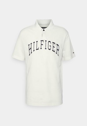 Polo blanc à manches courtes avec texte noir "HILFIGER" sur la poitrine et un petit logo sur la manche gauche.