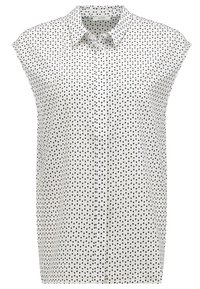 Vit ärmlös blus med små svarta fyrkantiga prickar, en spetsig krage och knäppning framtill.