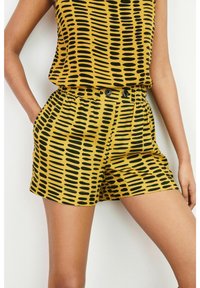 Pantalones cortos amarillos con un patrón abstracto negro, banda elástica en la cintura, dos bolsillos laterales y dos acentos de botones en el frente.