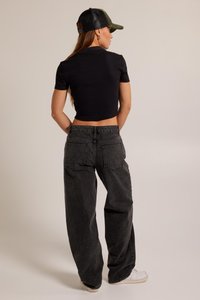 Black cropped t-shirt paired with high-waisted, loose-fitting dark gray jeans. Model wears a green cap and white sneakers.