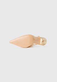 Chaussure à talon haut en cuir verni nude avec un bout pointu, une semelle texturée et un accent doré à l'arrière du talon.