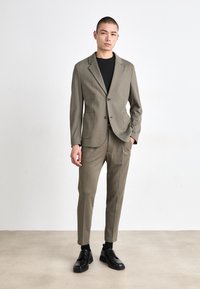 Lys grå dress med en to-knapps blazer og to frontlommer, kombinert med avsmalnende bukser og svarte sko. Glatt, formell stoff.