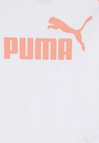 Balts T-krekls ar lielu korallkrāsas "PUMA" logotipu un lecoša kaķa grafiku. Kokvilnas materiāls, gluda tekstūra, kuplā kakla dizains.