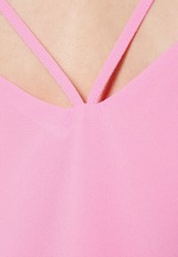 Pink sleeveless top featuring a smooth fabric texture, V-neckline, and crisscross strap design at the back.