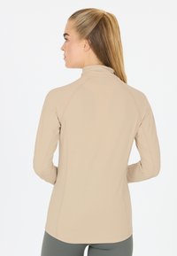 Beige langmouwtop met een hoge kraag, voorzien van raglanmouwen en een soepele, lichte stof. Opvallende naaddetails aan de achterkant.