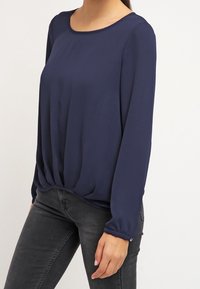 Námořnická modrá blůza s dlouhými rukávy a kulatým výstřihem, se nařasením v pase a knoflíkovými detaily na manžetách. Hladká textura.