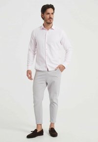 Chemise rose clair à manches longues avec devant à boutons, associée à un pantalon gris fuselé et des mocassins foncés. Tissu lisse, coupe ajustée.