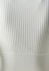 Bílá strukturovaná látka s vertikálním ribovaným vzorem, která má na spodní straně hladký horizontální pruh, vytvářející vrstevnatý vzhled.