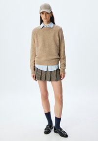 Beiger Pullover, hellblaues Hemd, karierter Minirock, marineblaue Socken, schwarze Slipper. Strukturiertes Strickmuster, lässige Passform und gestapelter Look mit Faltendetail.