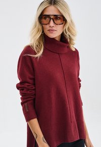 Bordowy sweter dziany z golfem, z długimi rękawami i ściągaczem na dole. Miękka faktura z luźnym krojem i bocznymi rozporkami.