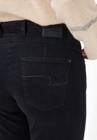 Jeans noirs à coupe slim, dotés d'une poche arrière avec un design en vagues et d'une étiquette en cuir texturé avec un motif d'étoiles sur la ceinture.