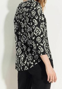 Blusa a maniche tre quarti in bianco e nero con motivo a gettito, caratterizzata da design astratti e un tessuto testurizzato, orlo curvo e scollo tondo.