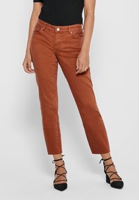Jean raccourci couleur rouille avec cinq poches, fermeture par bouton et légers effets de froissement. Assorti à des talons noirs à brides.