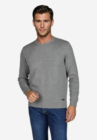Grau gestrickter Pullover mit Rundhalsausschnitt und gerippten Bündchen, kombiniert mit dunkelblauen Jeans. Verfügt über ein kleines schwarzes Markenschild am Saum.
