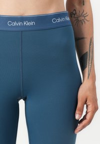 Navy tajice brenda Calvin Klein s glatkom teksturom, s elastičnom pasicom s brandom i prilagođenim krojem.