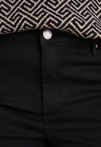 Jean en denim noir au design épuré, doté d'un bouton métallique et de détails de couture discrets. Le vêtement est assorti à un haut à motif.