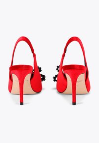 Czerwone zamszowe czółenka na pasku z wysmuklającym noskiem, otwartym tyłem i cienkim czarnym obcasem. Posiadają czarne dekoracyjne akcenty po bokach.
