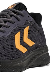 Szare buty sportowe z siateczkowej tkaniny, pomarańczowymi akcentami w kształcie chevronu i plamiście czarną podeszwą. Posiadają sznurowanie oraz teksturowe detale na cholewce.