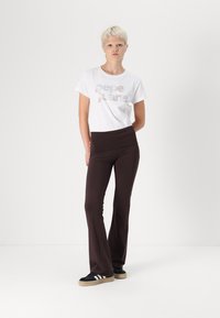 Hvid t-shirt med "pepe jeans" tekst i metalliske farver, parret med mørkebrune flarebukser og sorte sneakers med hvide striber.