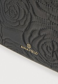 Czarna pikowana torebka z tłoczonym wzorem róż, złotym logo "ANNA FIELD", gładką fakturą i minimalistycznym designem.
