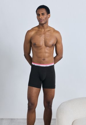 Boxers pour hommes noirs avec une ceinture rose et blanche portant le logo Nike. Le tissu est lisse, ajusté, d'une longueur mi-cuisse et sans motifs visibles.