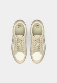 Paire de baskets BOSS beige et blanches avec lacets, logo BOSS visible à l'intérieur et sur la languette, sur un fond clair uni.