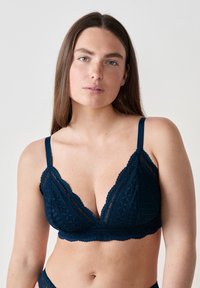 Brassière en dentelle bleu marine avec un décolleté festonné et une bande inférieure, ornée de motifs floraux et géométriques, avec des bretelles réglables et une texture douce.