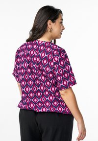 Kurzarmshirt mit lila-pinkem Muster und rhombusförmigen Formen. Hergestellt aus leichtem Stoff. Verfügt über eine lockere Passform und einen runden Halsausschnitt.